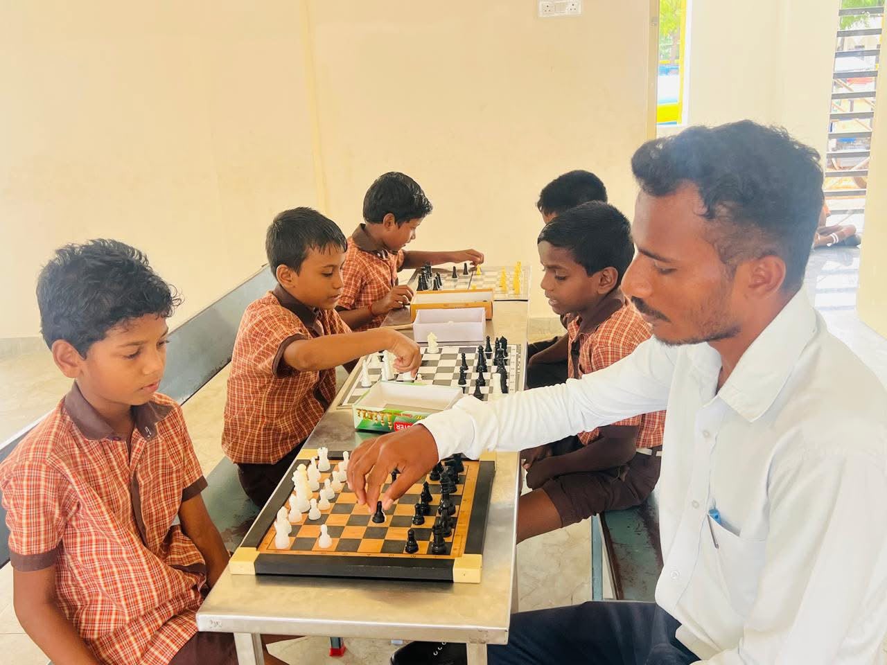 Coach teaching primary students how to play chess in the activity hall