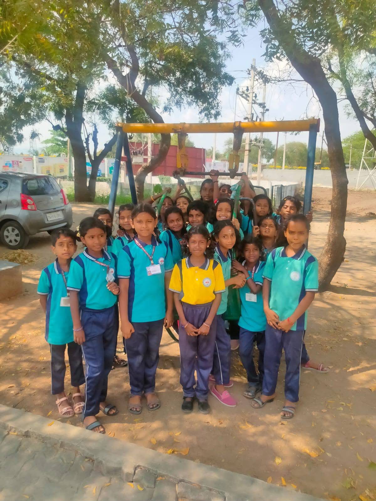 Group of primary students gathered around playground swings under the trees